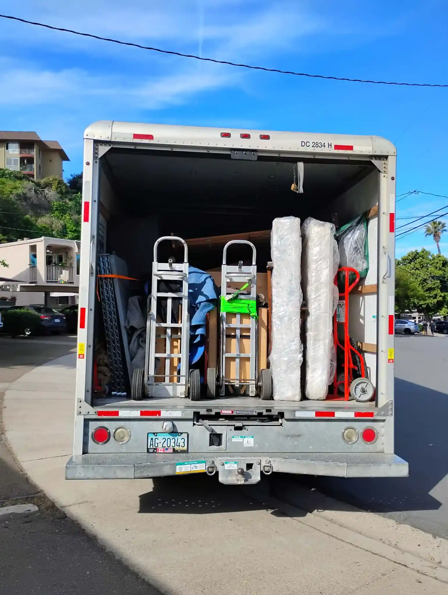 The open back of a Mudanza Moving Services truck showing securely strapped hand trucks and carefully wrapped mattresses loaded for transport.