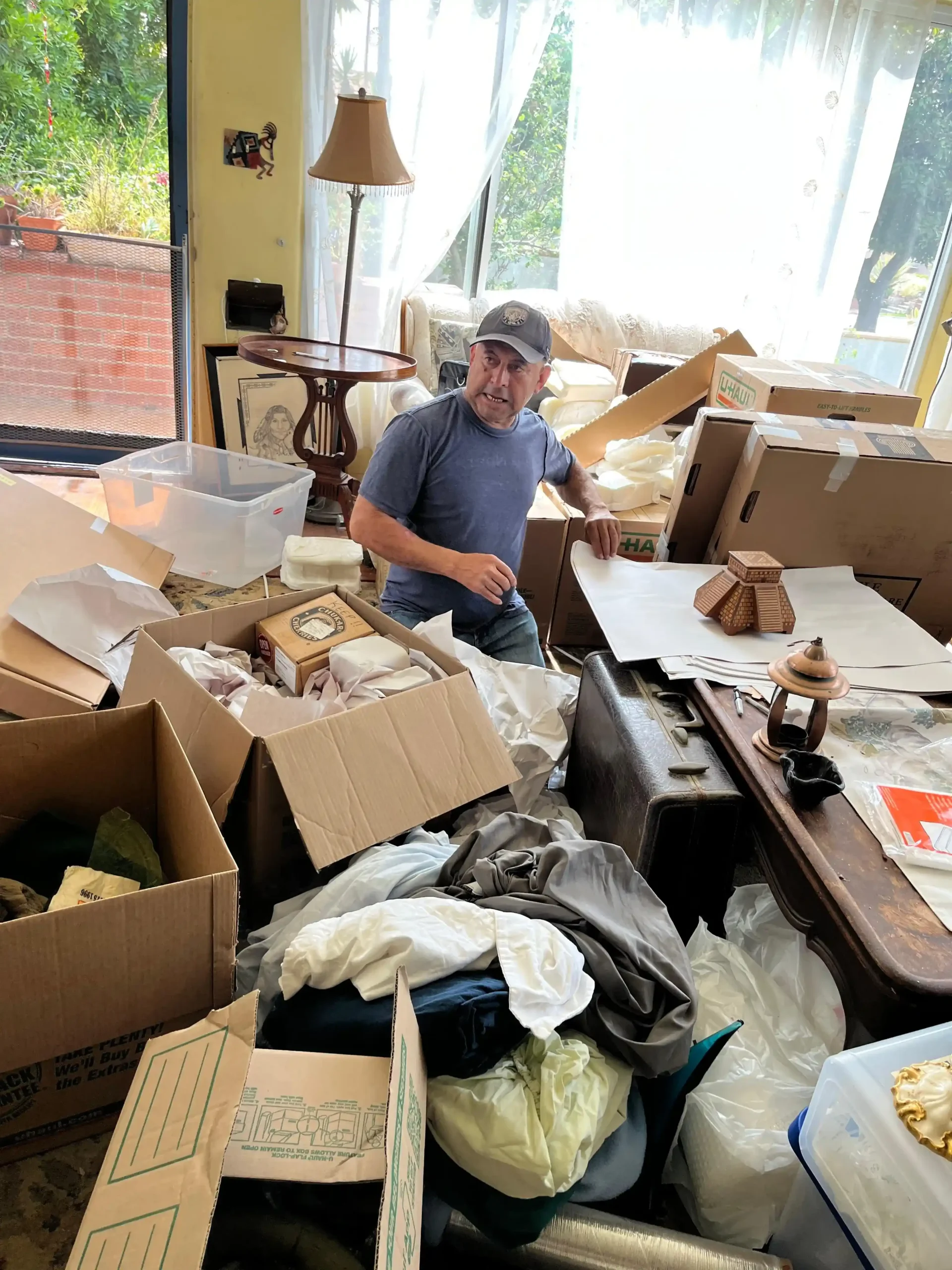 A Mudanza Moving Services team member carefully packing household items into boxes with protective paper in a bright living room.